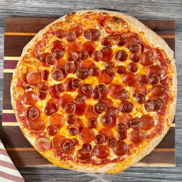 A whole Punxsy Pizza pepperoni pizza, with both large and small pepperonis, on a wooden cutting board.